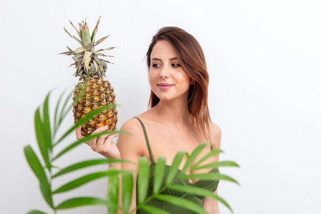 Portrait of young woman in swimsuit with pineapple and palm on white background. Summer season image concept