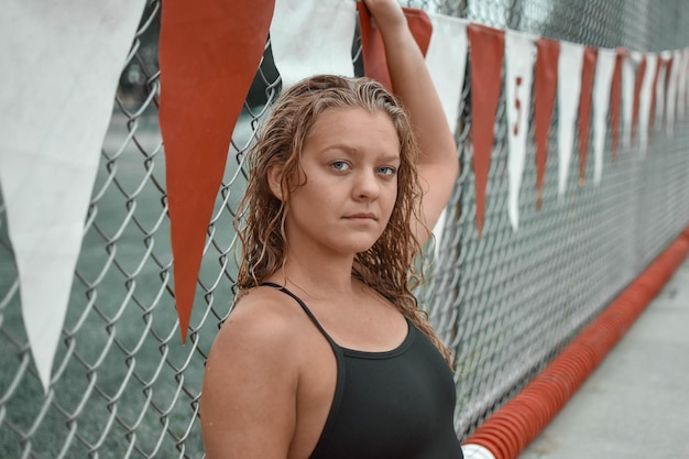 Photo portrait of young woman in swimwear by chainlink fence