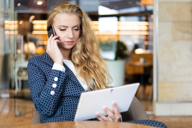 Portrait of a young woman talking on the phone on a break while using a digital tablet