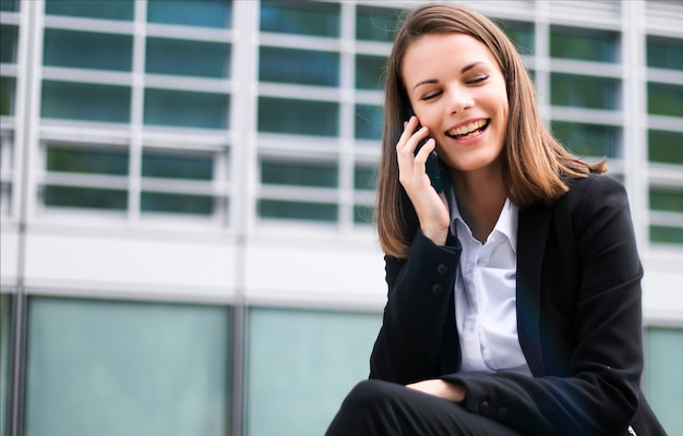 Portrait of a young woman talking on the phone sitting on a bench outdoor