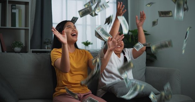 Portrait of a young woman and teenage girl enjoying scattering cash bills on a sofa in the living room at home