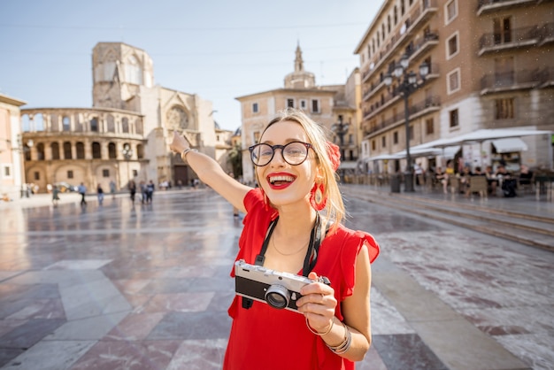 Portrait of a young woman tourist in red dress with hand fan on the central square of the old town in Valencia city, Spain