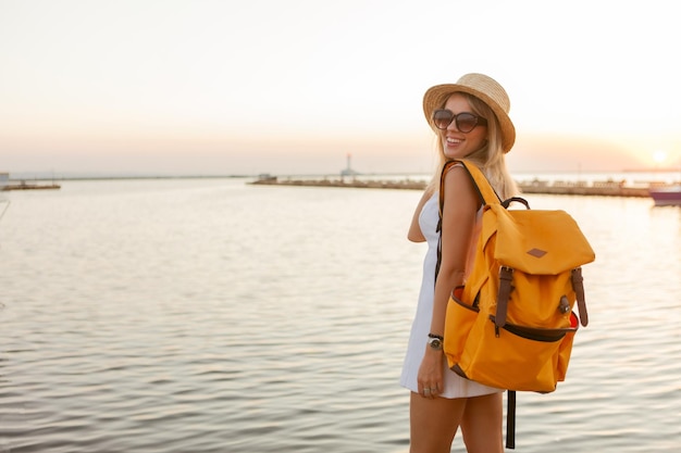 海の日の出で大きな旅行バックパックを持つ若い女性の観光客の肖像画。旅行と観光のコンセプト