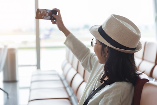스마트 폰으로 selfie를 복용하는 젊은 여자 여행자 착용 안경 및 모자의 초상화. 행복 하 게 웃는 여자 승객. 여행, 휴가 메이커.