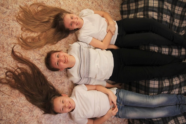 Portrait of young woman and two female teenagers lying on the floor at home, their feet on the couch, concept of family relations