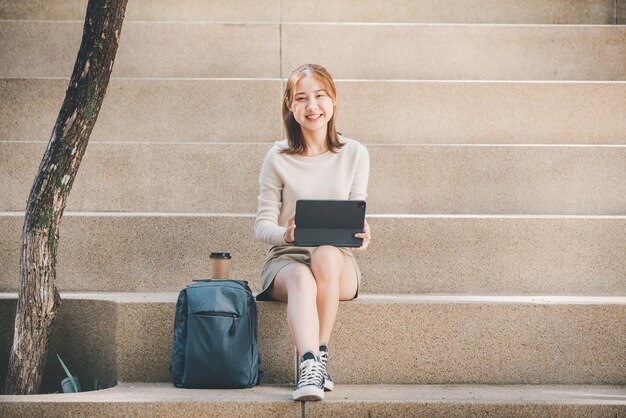 外の階段に座っているデジタルタブレットを使用する若い女性の肖像画