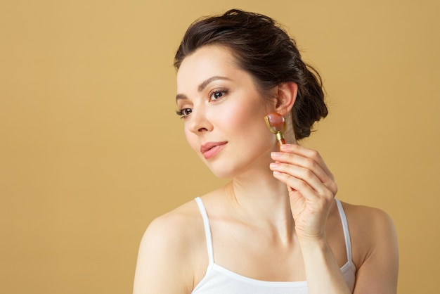 Portrait of a young woman using a facial massage roller made of natural rose quartz