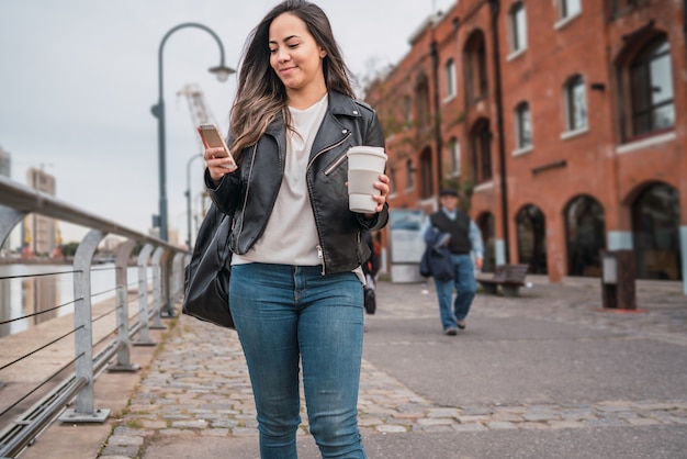 コーヒーを飲みながら歩いている間彼女の携帯電話を使用して若い女性の肖像画。