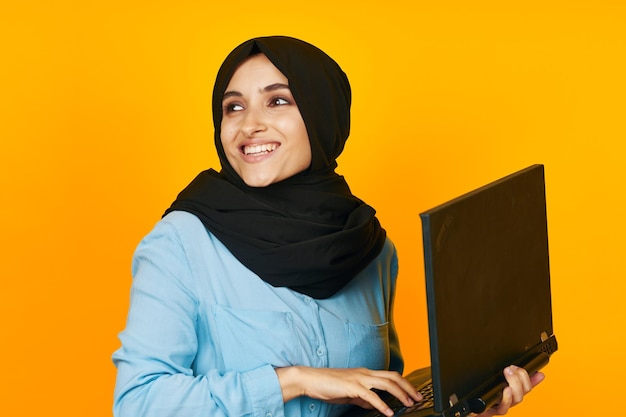 Portrait of young woman using laptop against yellow background