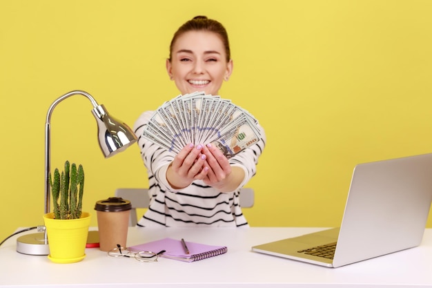 Portrait of young woman using laptop while sitting on table against yellow background