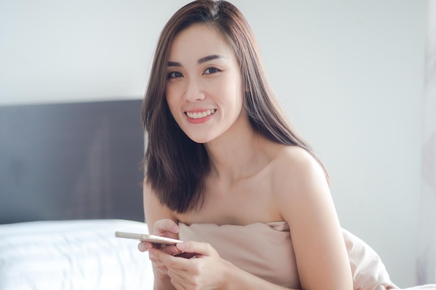 家のベッドに座って携帯電話を使っている若い女性の肖像画