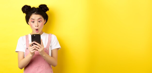 Portrait of young woman using mobile phone while standing against yellow background