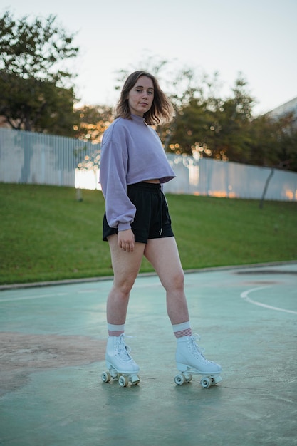 Portrait of a young woman using roller skates at a field during a sunset She is looking at camera