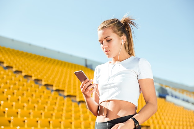 屋外スタジアムでヘッドフォンとスマートフォンを使用して若い女性の肖像画