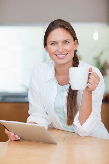 Портрет молодой женщины, используя планшетный компьютер во время питья кофе