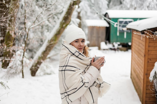 Portrait of young woman in warm clothes in winter forest Drinking hot tea outdoors from thermos Hiking Tourism