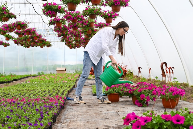 Foto ritratto di giovane donna che annaffia i fiori giovane donna adulta che lavora in serra e gode di bellissimi fiori