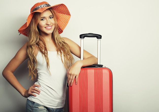 Portrait of young woman wearing big straw orange hat standing with orange travel bag