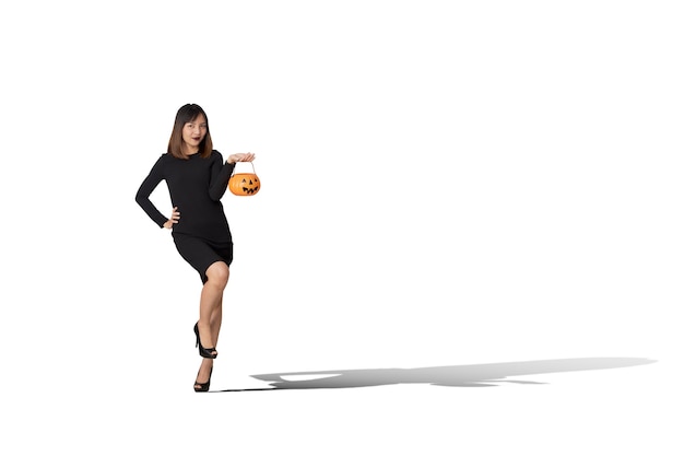 Portrait of a young woman wearing a black witch costume holds a pumpkin for a Happy Halloween party.