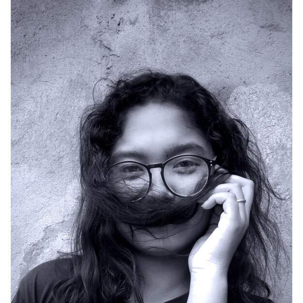 Photo portrait of young woman wearing eyeglasses while covering mouth with hair