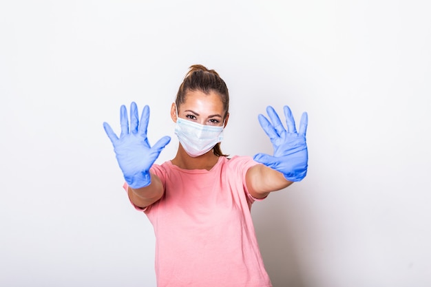 Portrait of young woman wearing face mask showing stop sign with both hands. Covid-19 prevention concept