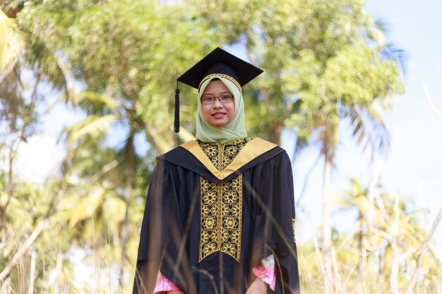 Foto ritratto di una giovane donna che indossa l'hijab e l'abito di laurea in piedi al parco