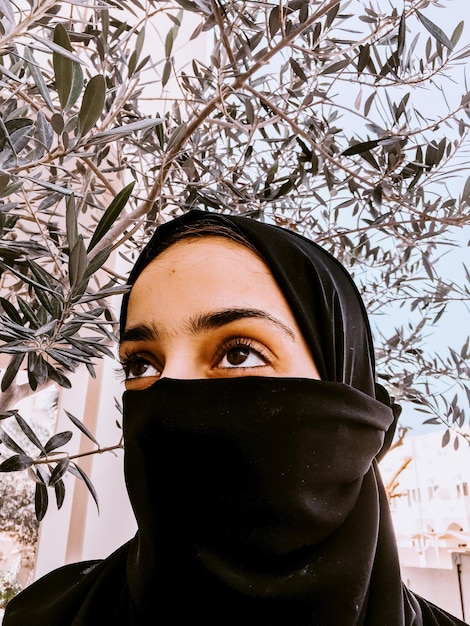 Foto ritratto di una giovane donna che indossa l'hijab e guarda lontano contro gli alberi