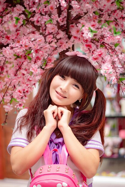 Foto ritratto di una giovane donna che indossa l'uniforme scolastica mentre si trova sotto i fiori di ciliegio rosa