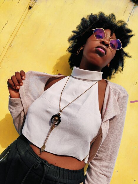 Photo portrait of young woman wearing sunglasses while standing against wall