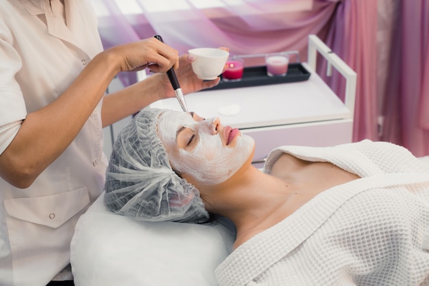 portrait of young woman while facial cosmetic procedure in spa salon