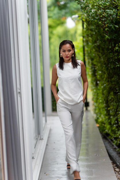 Portrait of a young woman in white clothes against the background of green plants after rain