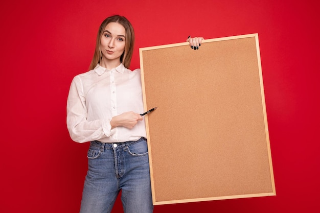 Portrait of a young woman in a white shirt holding a task board on a red background