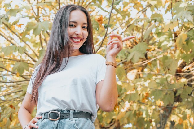 Portrait of a young woman on white shirt pointing next to her in a autumnal forest during autumn. Season concept, Blank space, copy space, looking away from camera