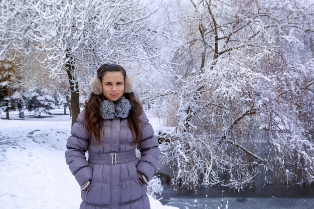 Il ritratto di una giovane donna in cuffia di inverno sta camminando nel parco dell'inverno