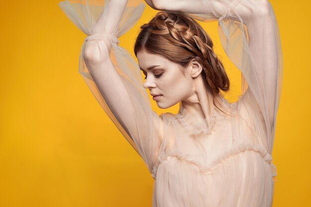 Portrait of young woman with arms raised standing against yellow background