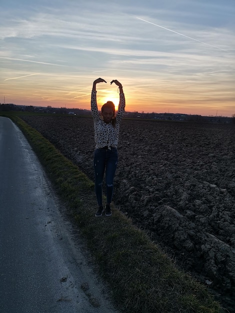 Foto ritratto di una giovane donna con le braccia alzate in piedi sul campo contro il cielo durante il tramonto