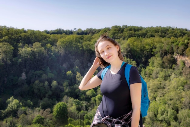 Photo portrait of young woman with backpack standing on mountain against clear sky during sunny day