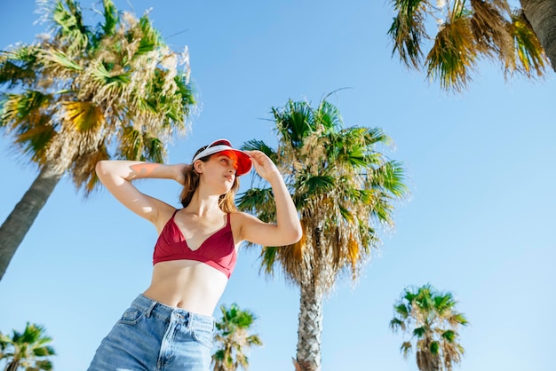 Portrait of young woman with bikini and sun visor with blue sky background and palm trees