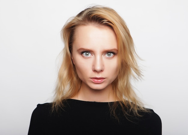 Portrait of a young woman with blond hair in a black shirt on a white background. A woman without makeup. Model test. Fashion model.