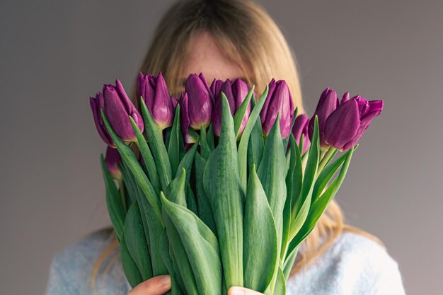 Portrait of a young woman with a bouquet of tulips on a gray background