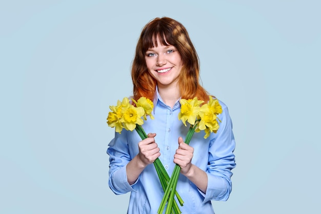 Portrait of young woman with bouquet of yellow flowers looking at camera