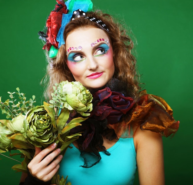 Портрет молодой женщины с ярким креативным макияжем, держащей сухие цветы в студии на зеленом фоне