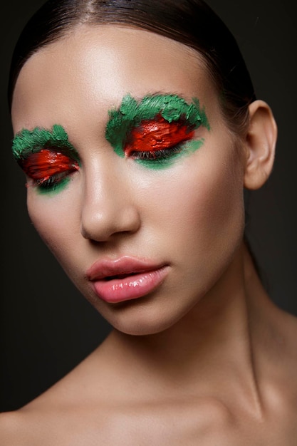 Portrait of young woman with bright red and green creative make up on dark background Beauty fashion