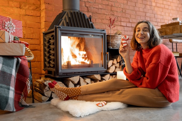 Ritratto di una giovane donna con una caramella di natale davanti al camino. accoglienza e calore della casa durante le vacanze invernali