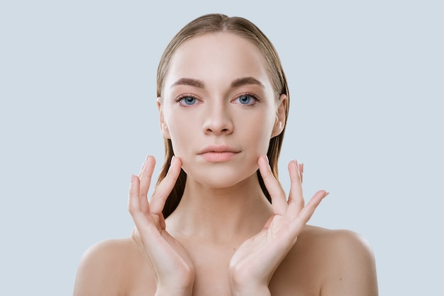 Portrait of a young woman with clean skin touches her face with her fingers on a light background