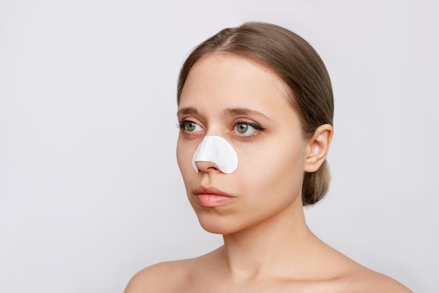 Portrait of a young woman with cleaning nose strips from\
blackheads or black dots on her skin