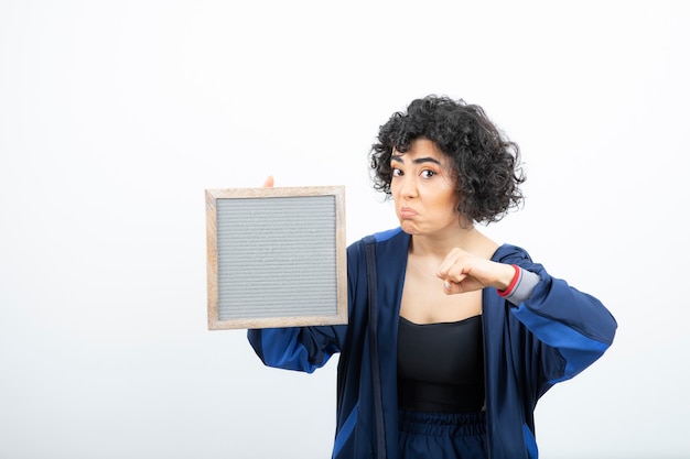 Portrait of a young woman with curly hair holding frame .