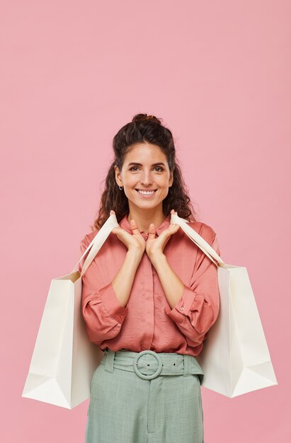 Portrait of young woman with curly hair smiling while holding the purchases against the pink background