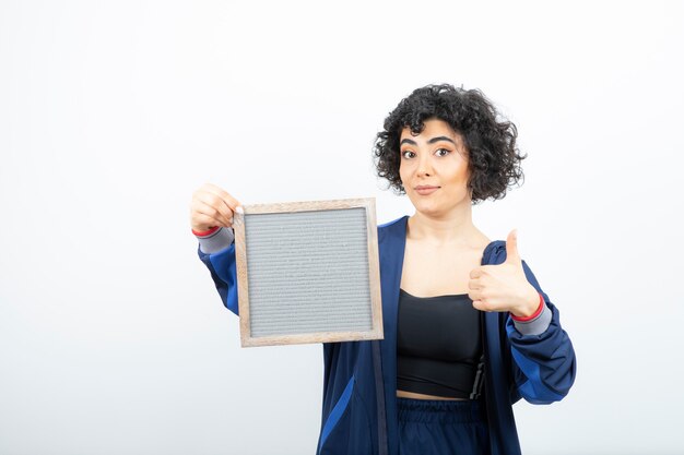 Portrait of a young woman with curly hair with frame giving thumbs up.