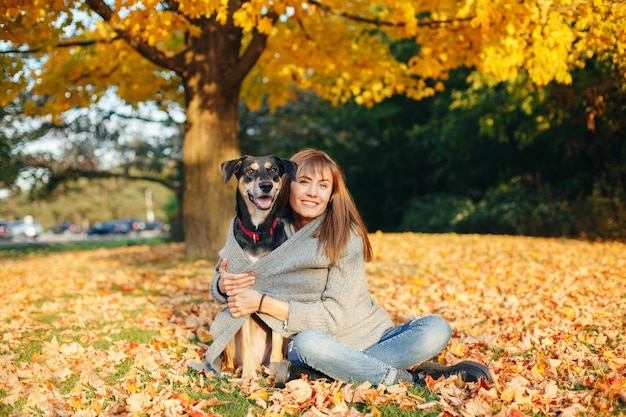 Portrait of young woman with dog sitting on leaves during autumn